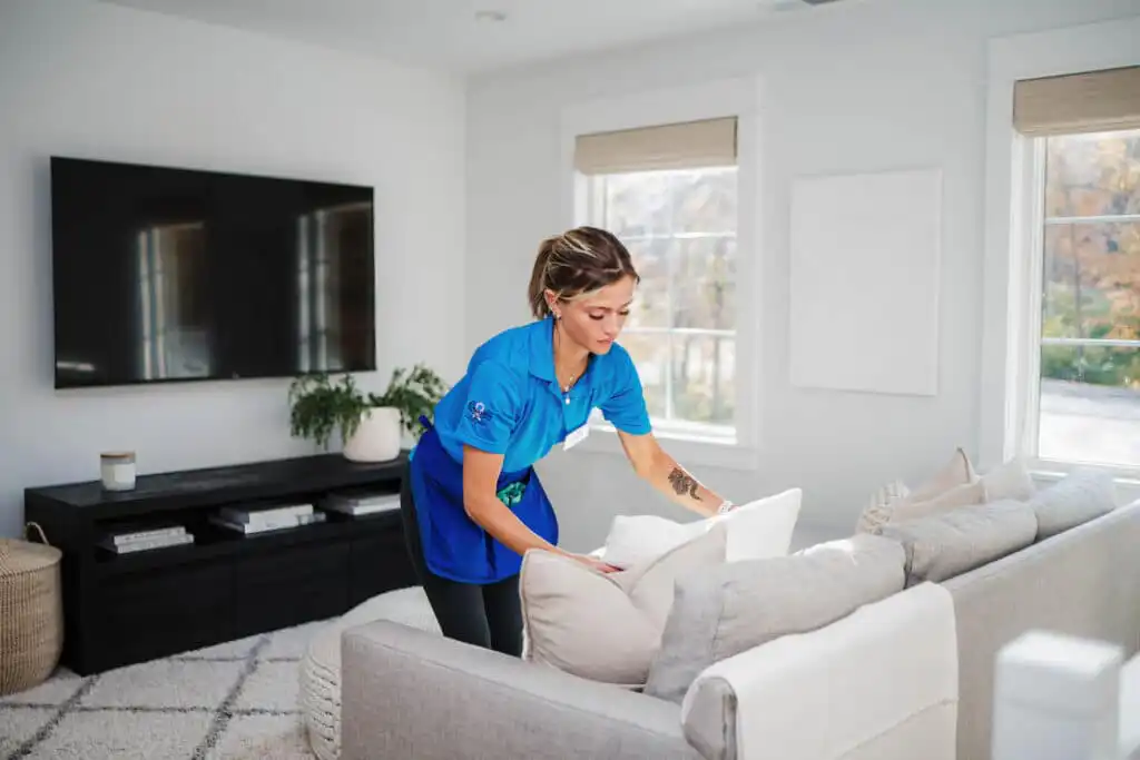A Best Day Housecleaning cleaner fluffing pillows during a cleaning visit.